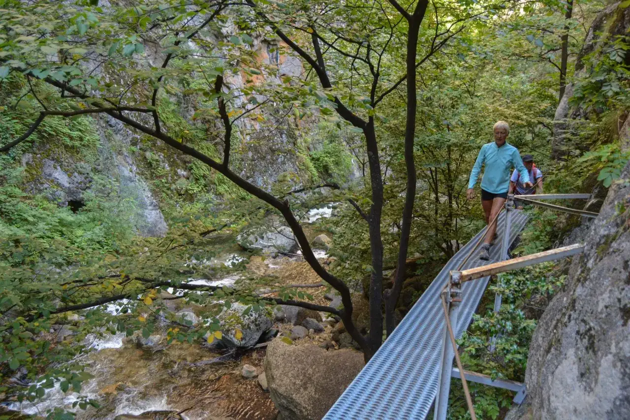 Randonneurs sur une passerelle m&eacute;tallique dans les gorges de la Caran&ccedil;a, au-dessus d'une rivi&egrave;re tumultueuse.