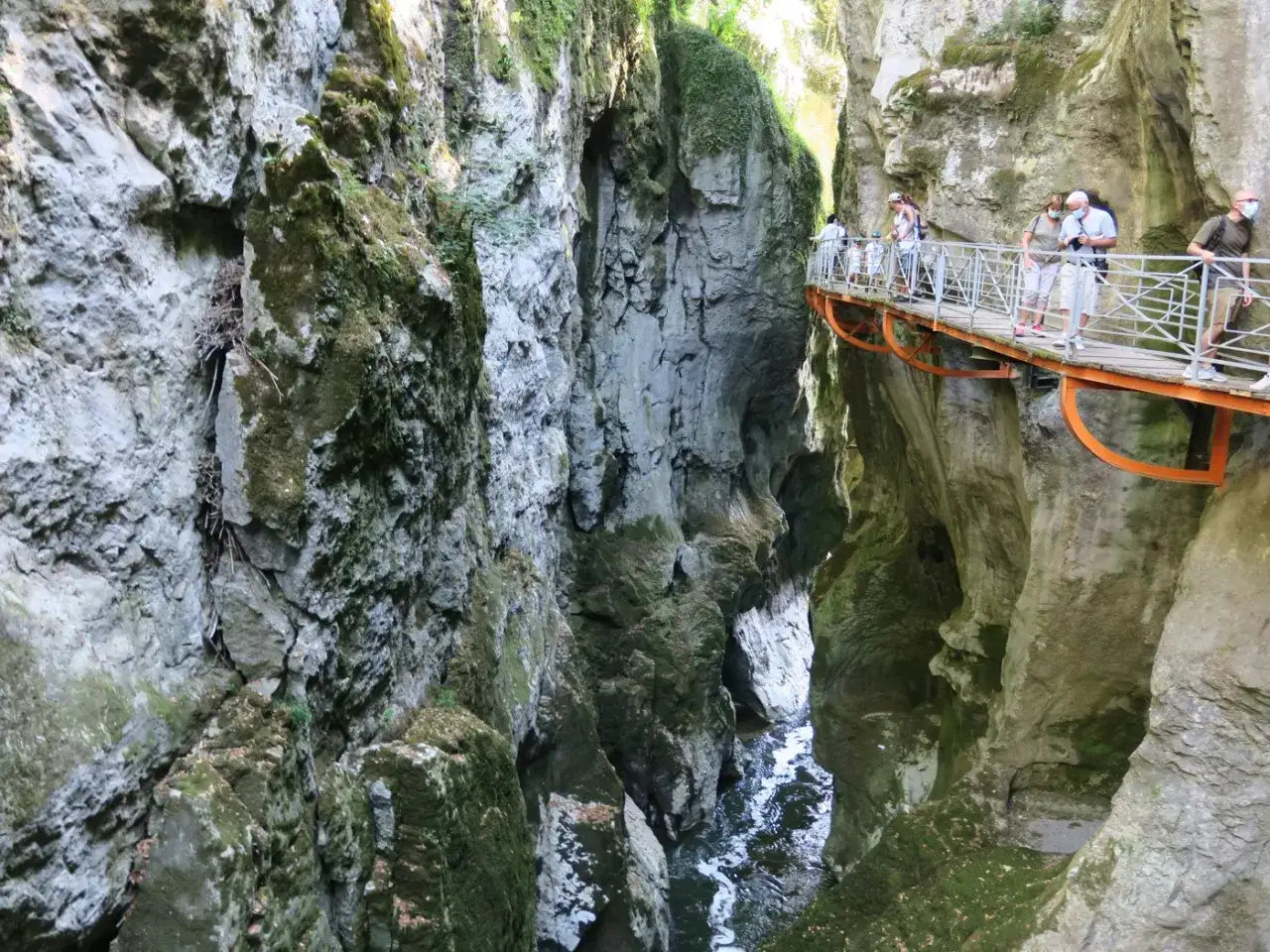 Des promeneurs admirent le paysage spectaculaire des gorges du Fier, une passerelle surplombant un cours d'eau encaiss&eacute; entre des falaises rocheuses.