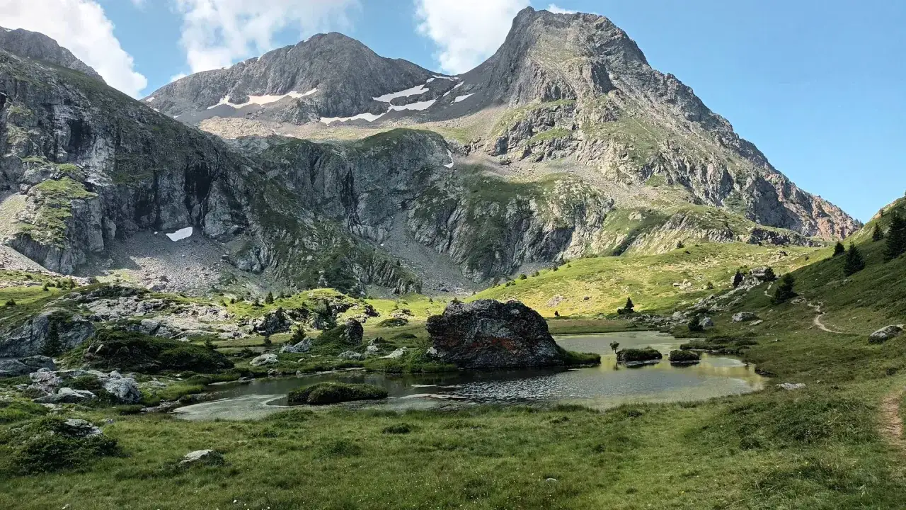 Le lac du Poursollet, un joyau alpin, reflète les montagnes majestueuses sous un ciel bleu. Un rocher imposant émerge de ses eaux paisibles.