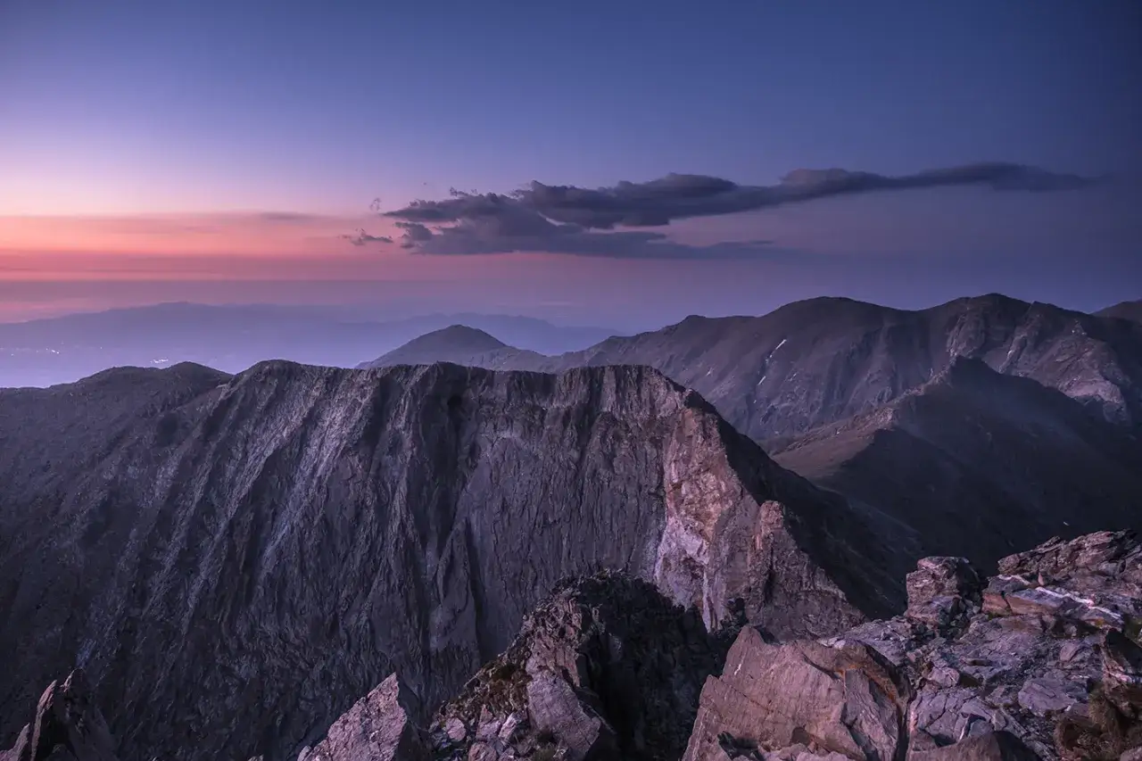 Le pic du Canigou se dresse majestueusement sous un ciel cr&eacute;pusculaire aux teintes roses et violettes. Les cr&ecirc;tes rocheuses d&eacute;chiquet&eacute;es s'&eacute;tendent &agrave; perte de vue.