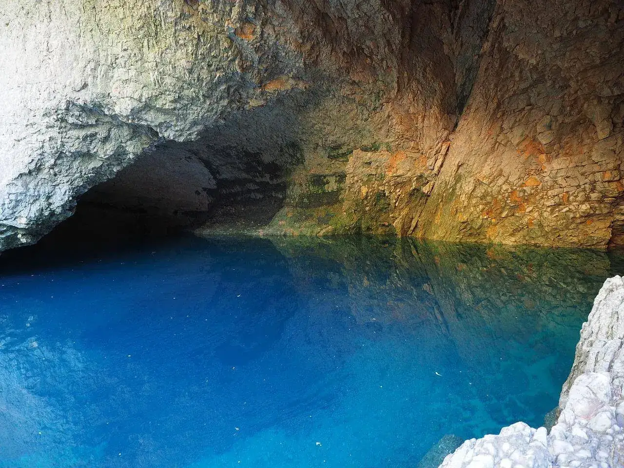 Le gouffre de la Fontaine de Vaucluse, une eau d'un bleu profond &eacute;mergeant d'une grotte aux parois rocheuses.