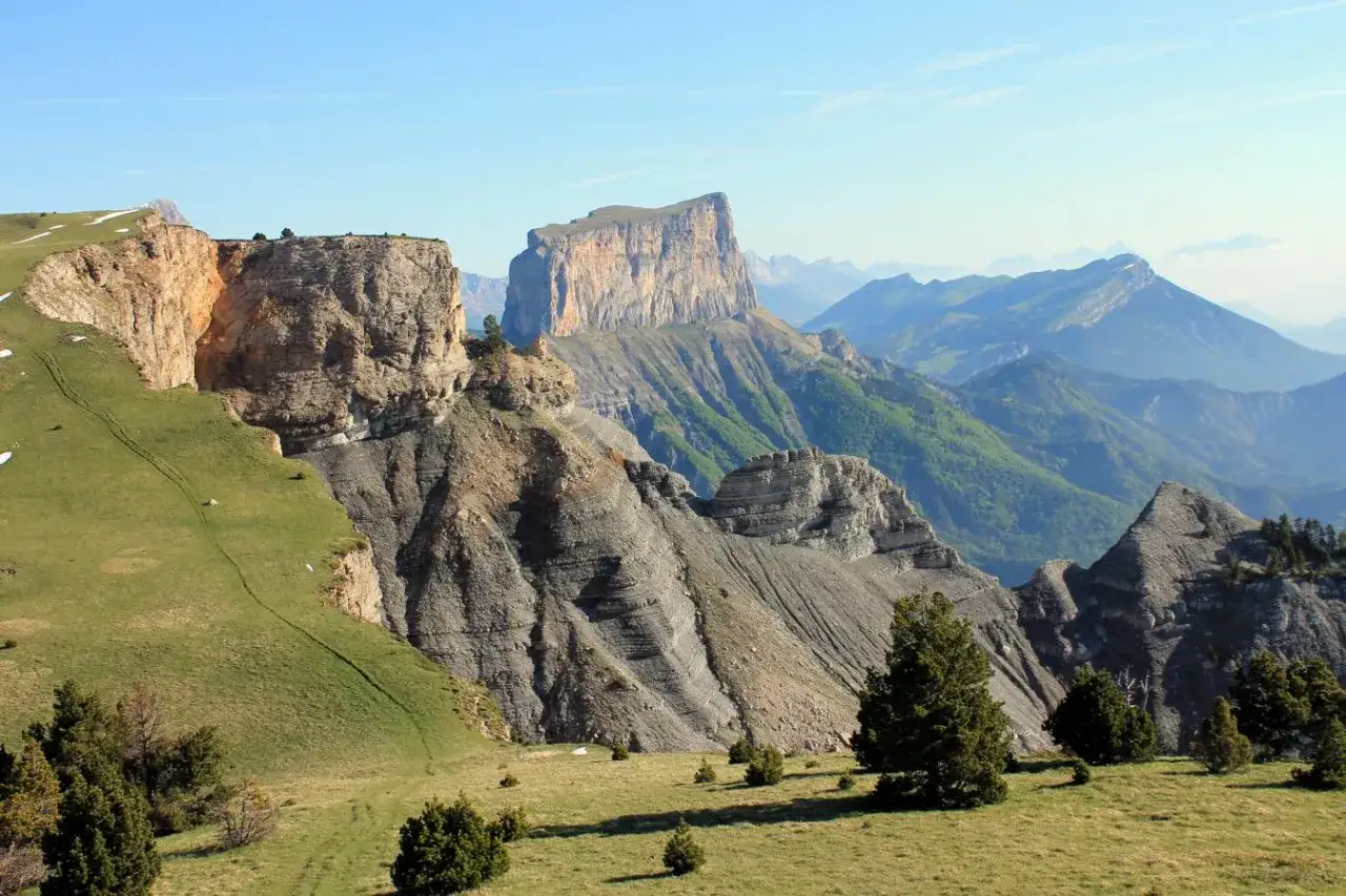 Vue panoramique sur la Grande Moucherolle, un paysage de falaises calcaires et de montagnes verdoyantes sous un ciel bleu clair.