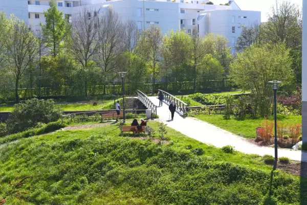 Promenade paisible aux prairies Saint-Martin à Rennes, avec un pont traversant un cours d'eau et des résidents profitant du soleil sur des bancs.