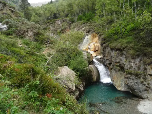 La cascade de l'Artigue dévale dans un bassin d'eau turquoise, entourée de roches et d'une végétation luxuriante.