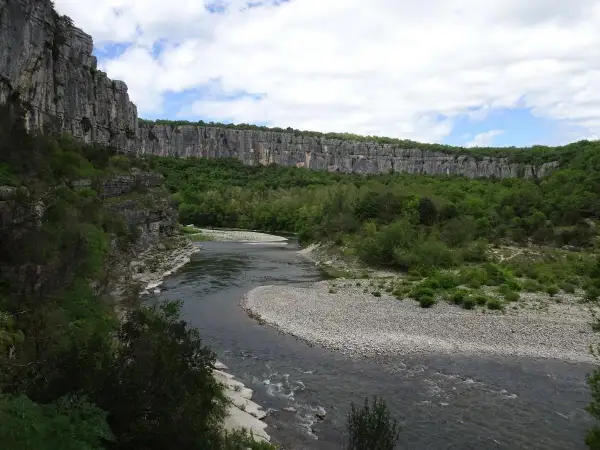 Rivière serpentant dans un cirque de falaises calcaires, le cirque de gens ruoms, bordé de verdure luxuriante.