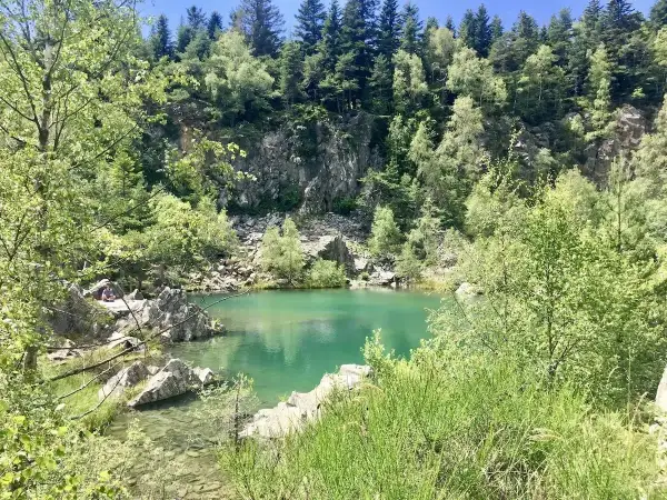 Un paisible lac bleu en Haute-Loire, entouré de rochers et d'une forêt verdoyante.