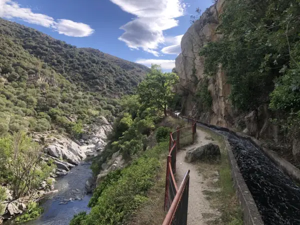 Sentier longeant un canal d'eau vive dans les gorges de la Guillera, avec une rivière en contrebas et des montagnes verdoyantes.