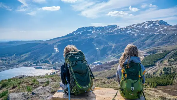 Deux randonneurs contemplent le paysage depuis le Puy de Chambourguet. Le lac scintille, les montagnes enneigées se dressent à l'horizon.