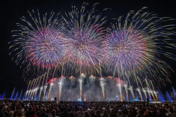 Spectacle de feu d'artifice sur le lac d'Annecy, illuminant le ciel nocturne de gerbes colorées au-dessus d'une foule admirative.