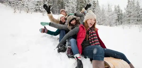 Des amis s'amusent en luge dans la neige, une scène joyeuse typique d'Annecy en décembre.
