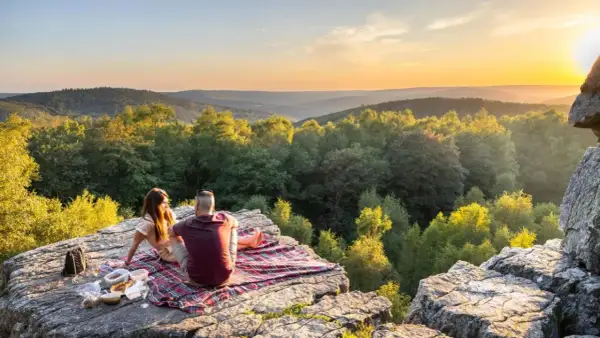 Un couple partage un pique-nique au coucher du soleil sur le roc la tour, surplombant une vallée boisée.