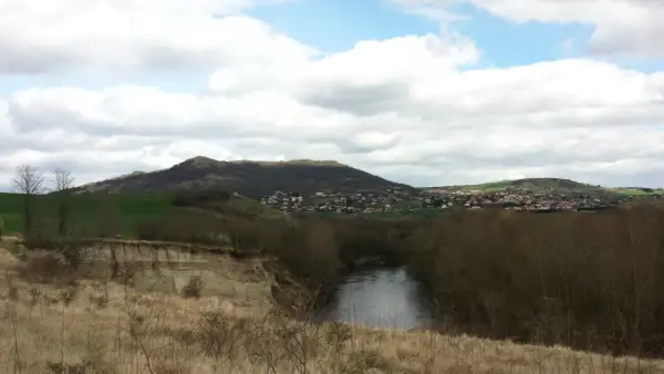 Vue panoramique d'une rivière sinueuse bordée d'arbres, avec une falaise de malmouche en contrebas et un village niché sur une colline verdoyante.