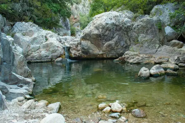 Un petit bassin d'eau claire aux Gorges d'Héric, avec une cascade tombant entre des rochers massifs. Une carte naturelle de ce lieu paisible.