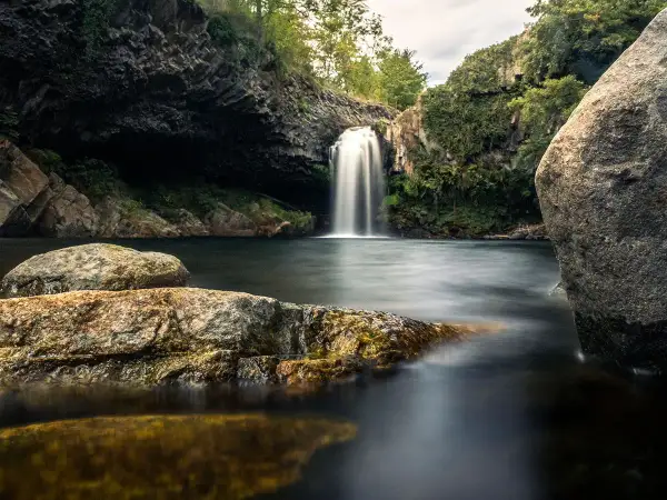 Magnifique cascade piscine naturelle en Ardèche, entourée de rochers et de végétation luxuriante. L'eau tombe en voile blanc dans le bassin sombre.