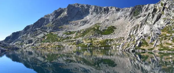 Reflets parfaits des montagnes rocheuses sur le lac de Bastani, sous un ciel bleu éclatant.