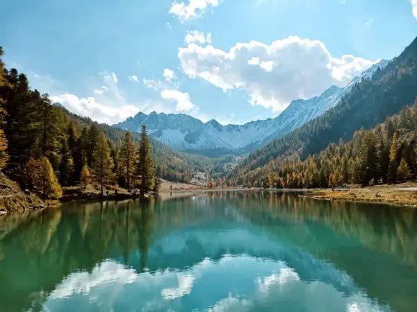 Le lac de l'Orceyrette, miroir des montagnes enneigées et des forêts d'automne, sous un ciel bleu éclatant.