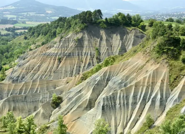 Le ravin de Corboeuf, un paysage spectaculaire aux strates colorées sculptées par l'érosion, dominé par une forêt verdoyante.