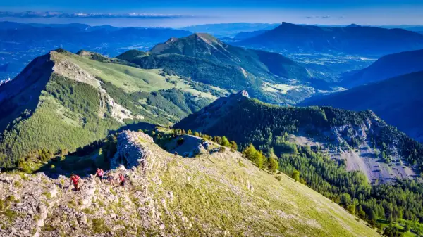 Randonneurs sur la crête rocheuse menant au pic de Gleize, avec des montagnes verdoyantes et un ciel bleu.