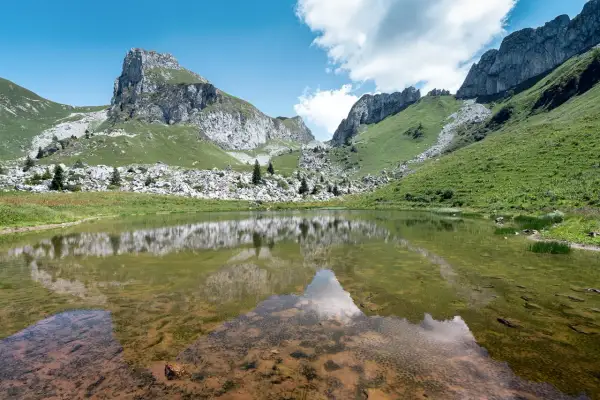 Le lac de Darbon, paisible, reflète les montagnes verdoyantes et rocheuses sous un ciel bleu et nuageux.