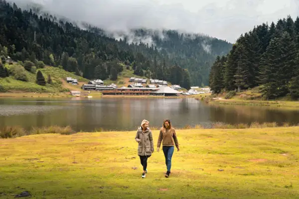 Deux amies profitent d'une promenade au bord du lac de Payolle, entouré de forêts et de montagnes brumeuses.