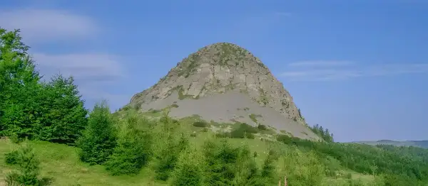 Le rocher de Sampzon, imposant et rocheux, se dresse sous un ciel bleu. Des arbres verts l'entourent.