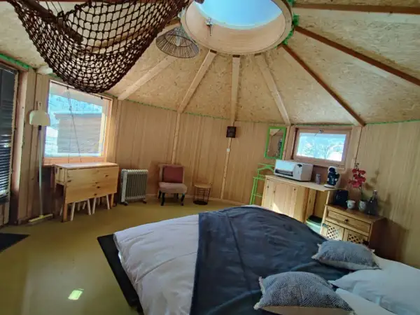 Intérieur douillet d'une yourte au col du Festre, avec un lit confortable, une kitchenette et une vue sur la nature.