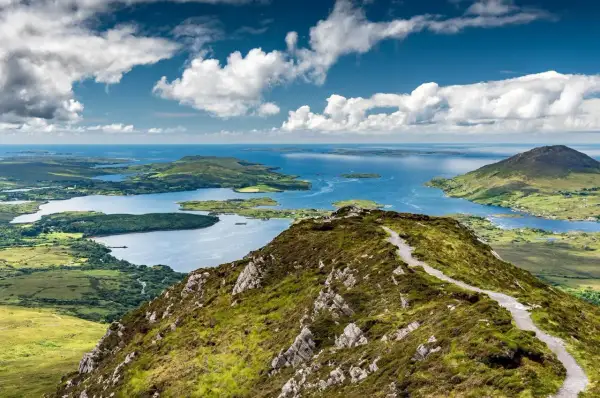Vue panoramique du lac du Connemara, un lieu d'une beauté sauvage avec des montagnes verdoyantes et des eaux bleues scintillantes sous un ciel nuageux.
