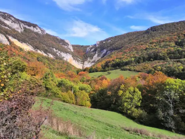 Vallée automnale aux couleurs vives, menant à la cascade de Chaudeyrolles. Le ciel bleu contraste avec les falaises et les arbres aux teintes orangées et vertes.