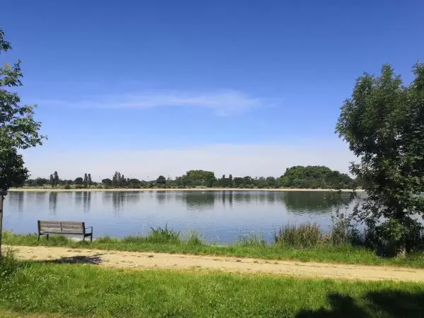 Un banc invite à la contemplation du lac de la Ramée sous un ciel bleu.